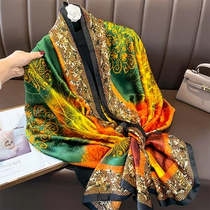 Elegant emerald and orange silk scarf with vintage floral prints on a leather sofa