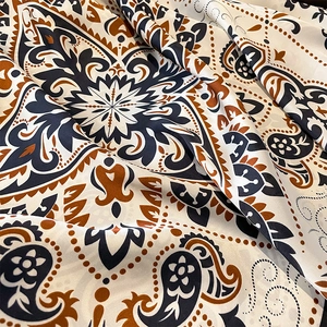 Dettaglio del tessuto setoso della sciarpa con motivi paisley e mandala blu e arancio