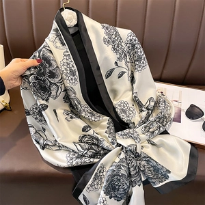 Elegant black and white floral print silk scarf displayed on a vintage leather sofa