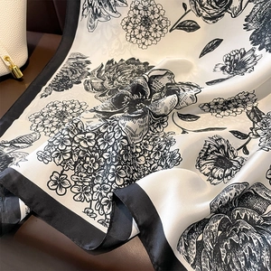 Elegant black and white floral silk scarf displayed with luxury bag and smooth texture
