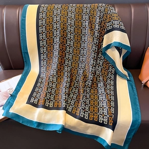 Elegant geometric print silk-like scarf with green border draped on a leather sofa