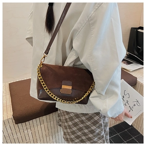 Détail du sac bandoulière en daim marron avec chaîne dorée et boucle sur un mannequin