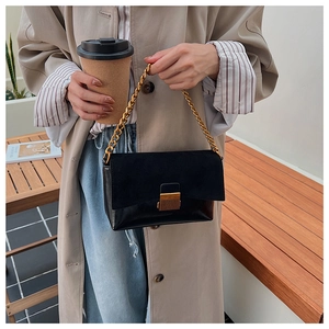 Détail du sac vintage en daim noir avec chaîne dorée sur un élégant manteau beige
