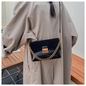 Détail du sac noir en daim et cuir lisse avec chaîne dorée porté par mannequin