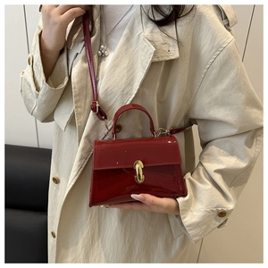 Detailed close-up of glossy red patent leather handbag with gold clasp and top handle