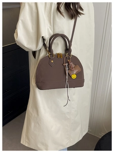 Dettaglio di una borsa marrone a forma di conchiglia indossata con cappotto beige
