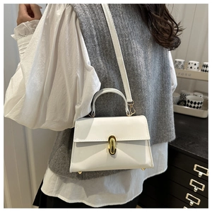 Polished white patent leather trapezoid handbag with gold twist lock on a model
