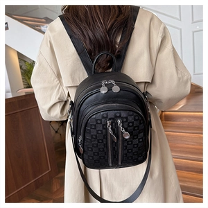 Detail of black faux leather backpack with checkerboard texture and silver zippers on a model