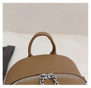 Detail of soft brown leather backpack featuring dual metal zippers and reinforced top handle