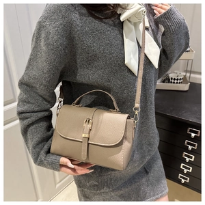 Detail of khaki pebbled leather crossbody bag with gold buckle and top handle on model