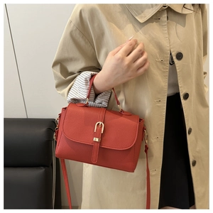 Detail of red litchi texture handbag with gold buckle and adjustable shoulder strap