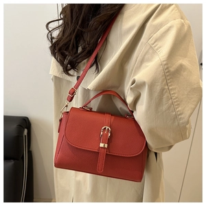 Close-up of red lychee grain leather crossbody bag worn with a beige trench coat