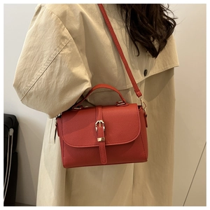 Red lychee textured crossbody bag with gold buckle styled on a beige trench coat