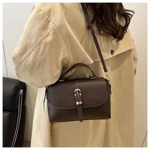 Detail of dark brown lychee textured handbag with gold buckle on beige trench coat