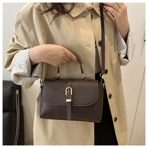 Detail of coffee brown pebble leather handbag with gold metal clasp on a beige trench coat