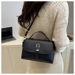 Detail of a black pebbled leather crossbody bag with gold buckle and adjustable strap