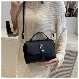 Detail of black pebbled leather handbag featuring golden buckle and round handle