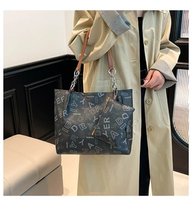 Close-up of black leather tote bag featuring letter print and chain strap detail
