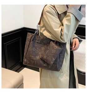 Detail of the brown tote bag featuring letter prints and elegant metal chain strap detail