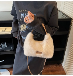 Detail of cream plush handbag with brown leather strap and brand tag in lifestyle setting
