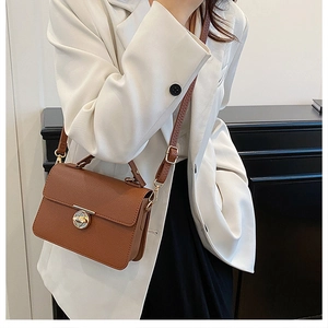 Close-up of brown pebbled leather handbag with gold metal twist lock on a shoulder strap