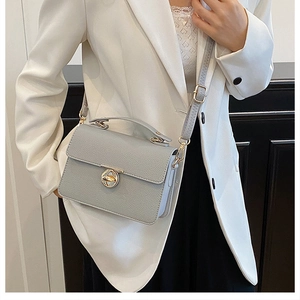 Detail of light gray textured leather crossbody bag with a gold metal rotary lock