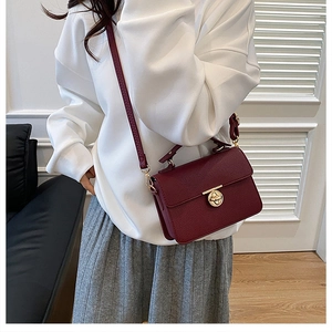 Detail of burgundy cross-body bag showing lychee grain texture and gold rotary lock