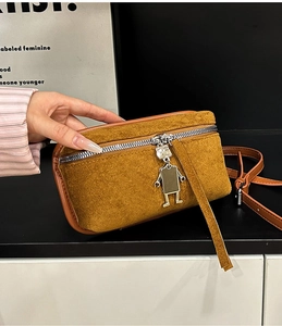 Detail of vintage suede crossbody bag featuring a unique robot charm and silver zipper