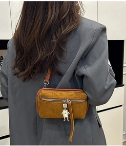 Detail of yellow faux suede crossbody bag with silver robot charm on grey blazer