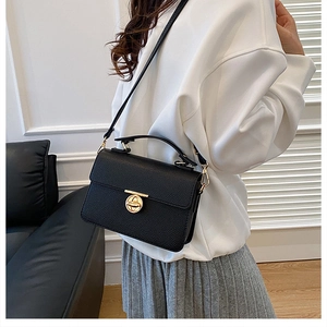 Model showing a black pebble leather crossbody bag with a gold round twist lock