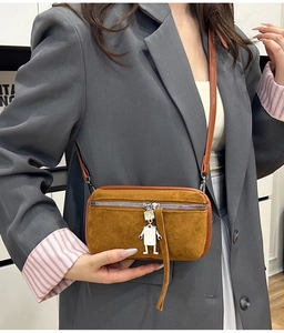 Detail of yellow suede crossbody bag with robot charm and long fringe on silver zipper