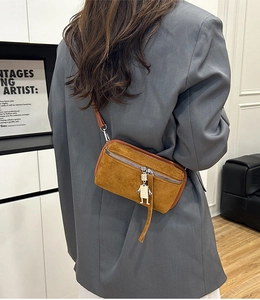 Detail of tan suede crossbody bag with silver robot charm and smooth metal zippers