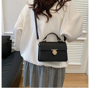 Close-up of black lychee grain texture and gold metal buckle on a shoulder bag