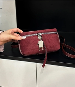 Detail of burgundy suede crossbody bag featuring a unique silver robot zipper charm