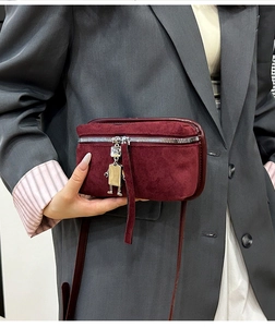Detail of burgundy suede crossbody bag featuring a silver robot charm and metal zipper