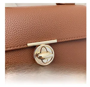 Detail of golden round twist lock on brown litchi pattern leather handbag surface