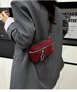 Detail of burgundy suede mini crossbody bag featuring a silver robot charm and zipper pull