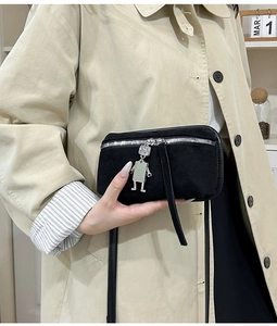 Detail of suede crossbody bag featuring silver zipper and robot charm accessory