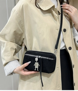 Close-up of suede crossbody phone bag with robot charm worn with a beige trench coat