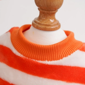 Macro shot of orange and white striped pet sweater with ribbed collar on wooden stand