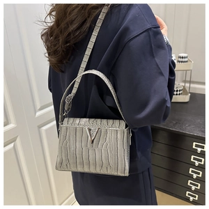 Detail of light grey crocodile pattern handbag featuring a metallic V-shaped clasp