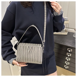 Detail of grey crocodile pattern handbag with silver V-shaped buckle and crossbody strap