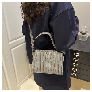 Detail of light grey crocodile pattern crossbody bag with silver V-shaped logo on a model