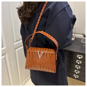 Detailed view of crocodile embossed leather texture and silver V-logo on brown handbag