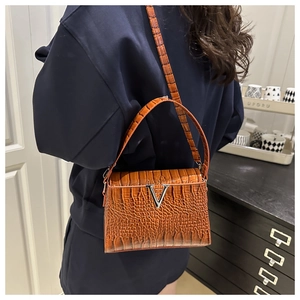 Brown crocodile embossed handbag with V-shaped metal clasp worn on the shoulder