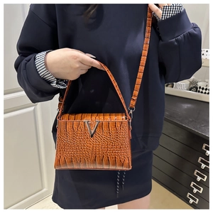 Detail of a brown crocodile pattern handbag featuring a silver V-shaped metal clasp buckle