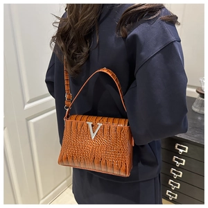 Detail of brown crocodile pattern handbag featuring a metallic V-logo and sleek strap