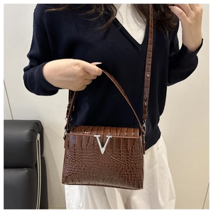 Detail of a brown croc-embossed handbag featuring a silver V-shaped metal buckle clasp