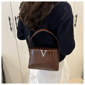 Detail of brown crocodile pattern leather handbag with silver V-logo and flap closure