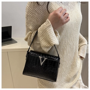 Close-up of black crocodile pattern leather handbag with silver V buckle on a beige sweater